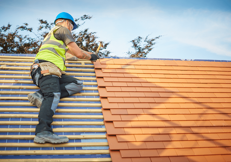 Roofer installing red tiles on roof