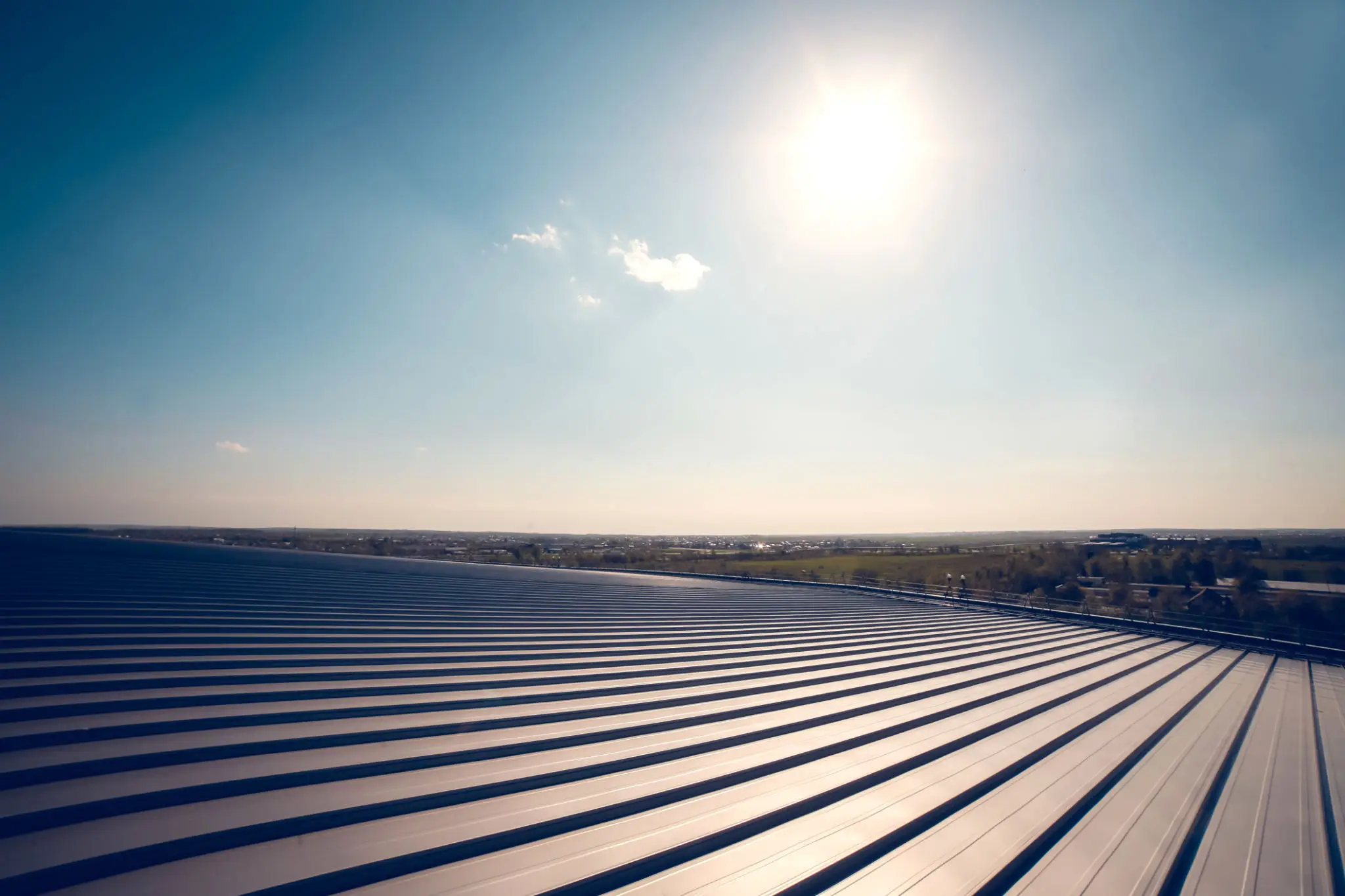 Sun shining brightly over a corrugated metal roof with clear blue sky.