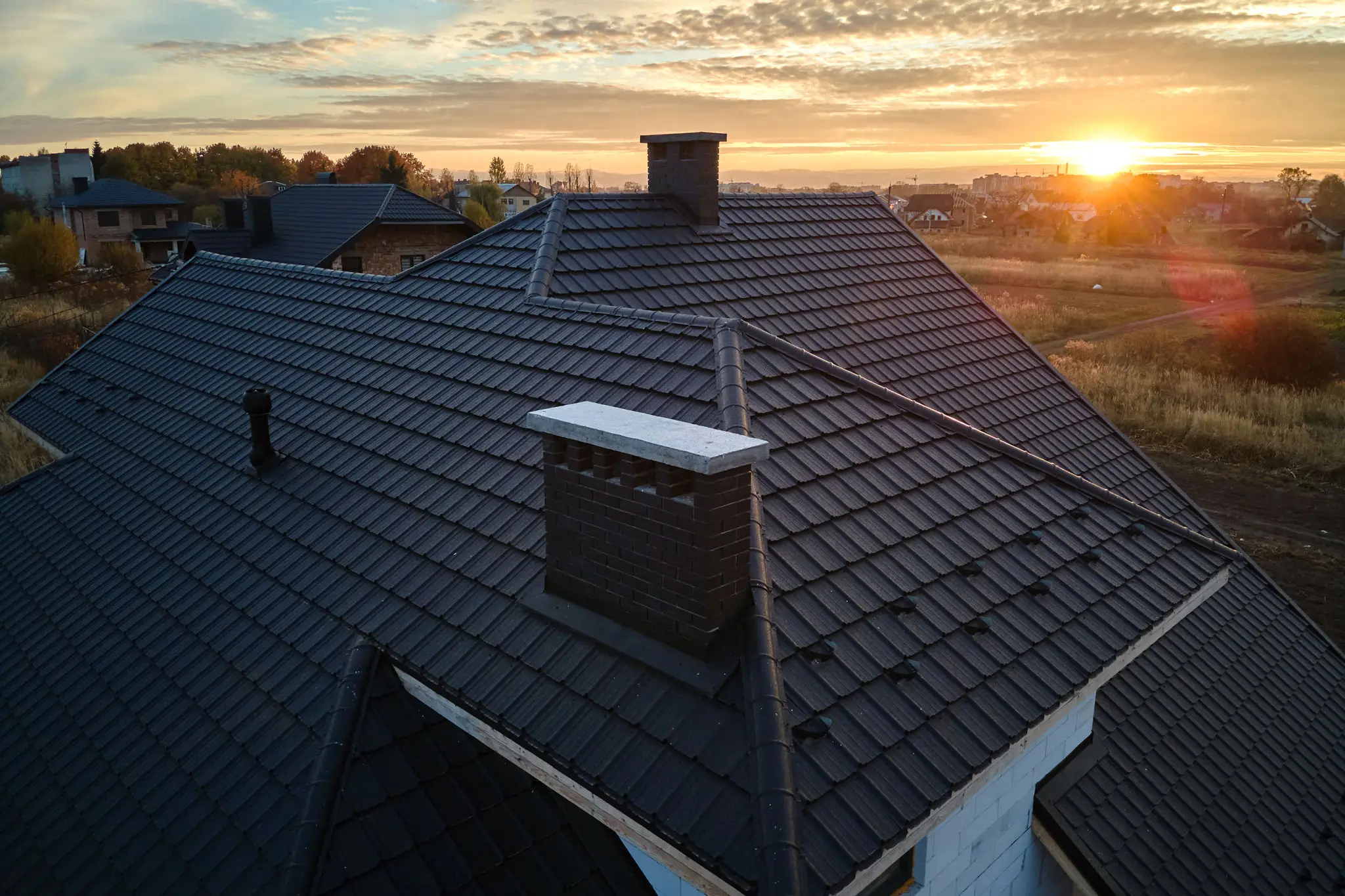 Sunset over a dark shingled rooftop with a chimney.